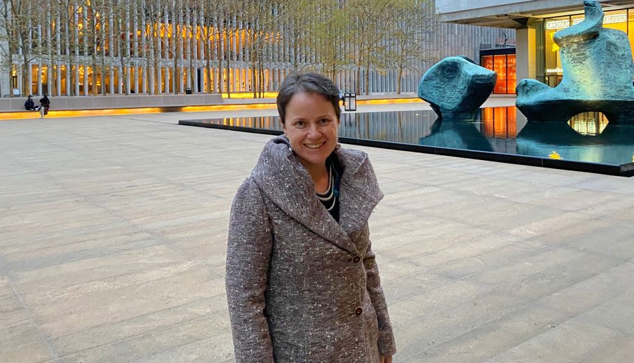 A woman smiling in front of a sculpture and building