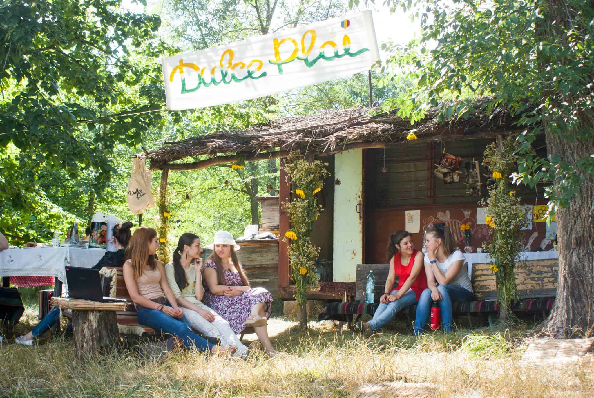 A group of young people sitting around in front of a cabin among woodland