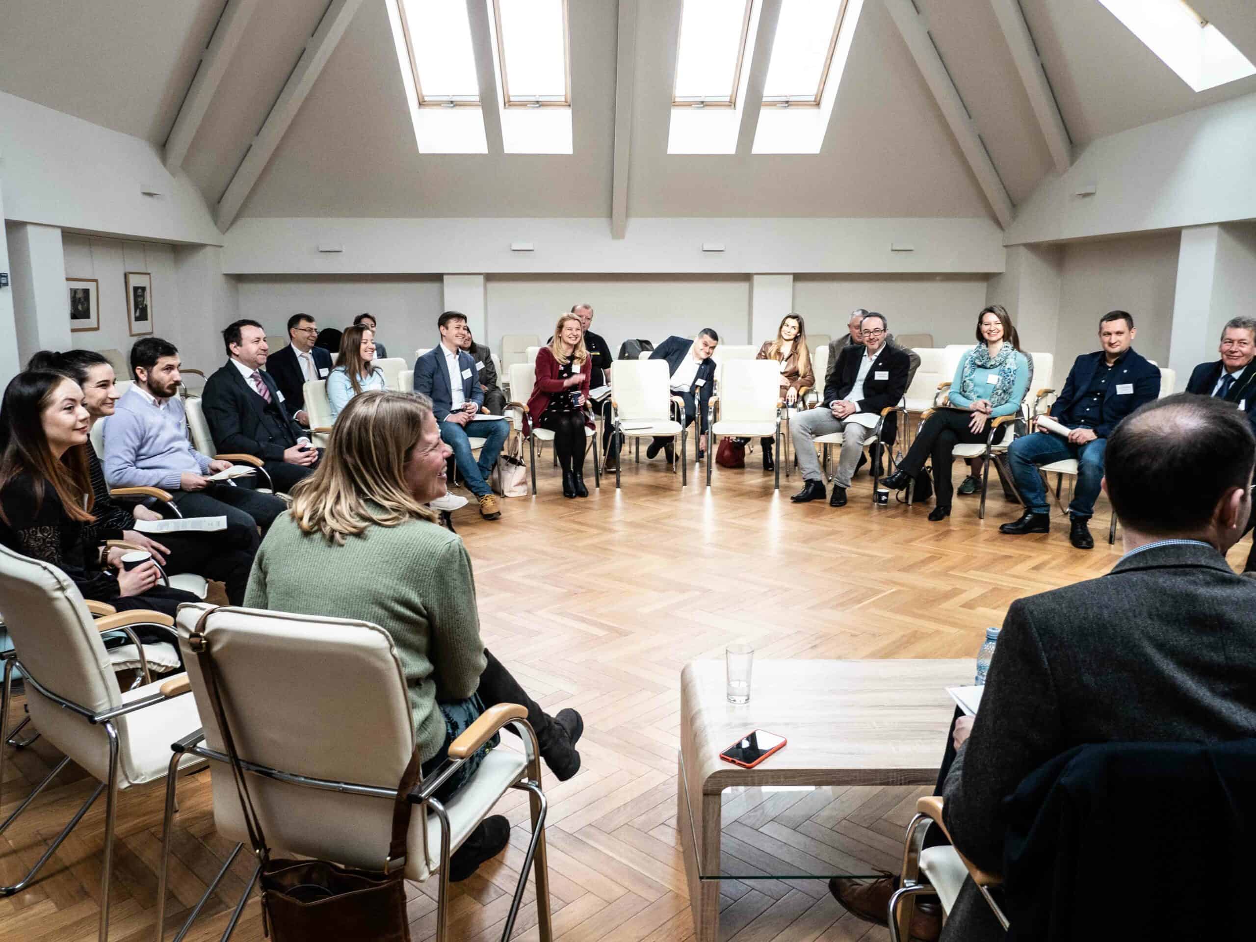 Men and women in a large room, sitting on chairs in a circle