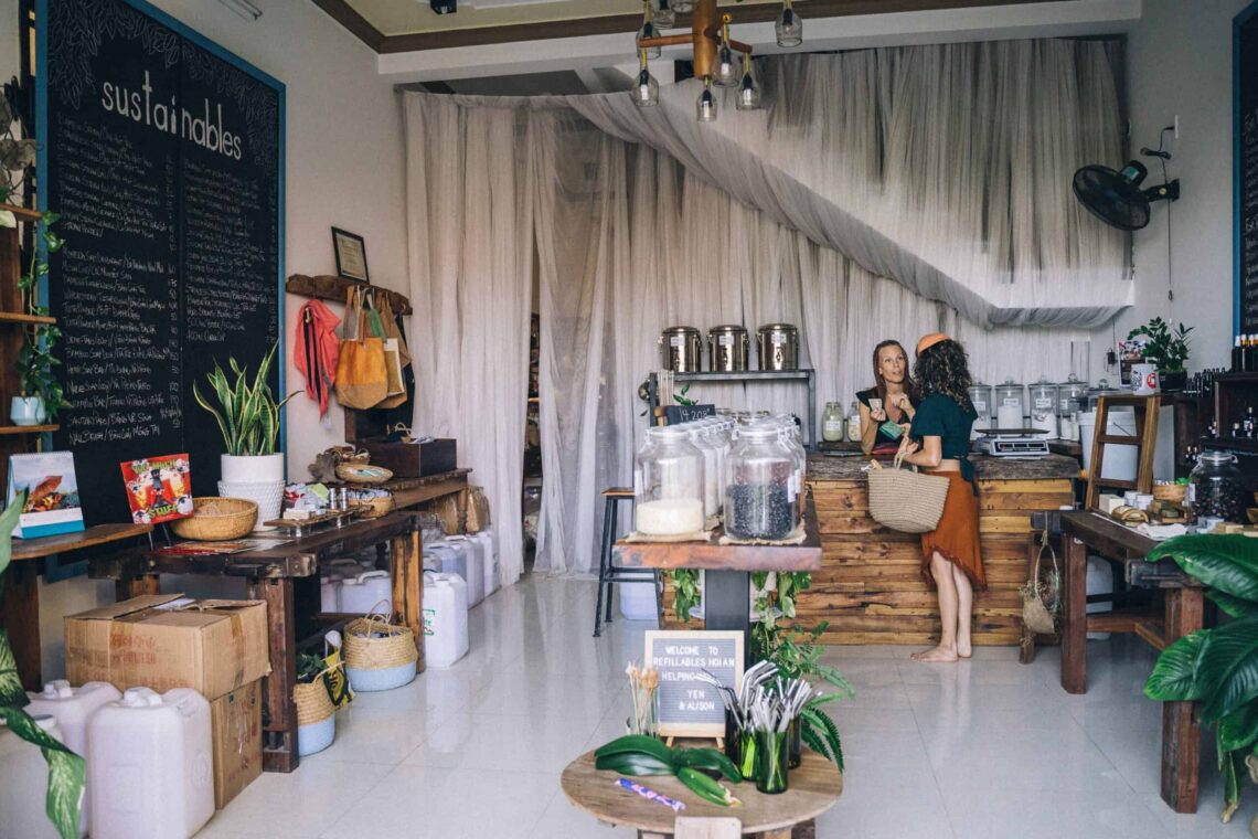 A photo of a cafe with a woman serving a customer at the bar. A blackboard on the left with 'Sustainables' written on it.