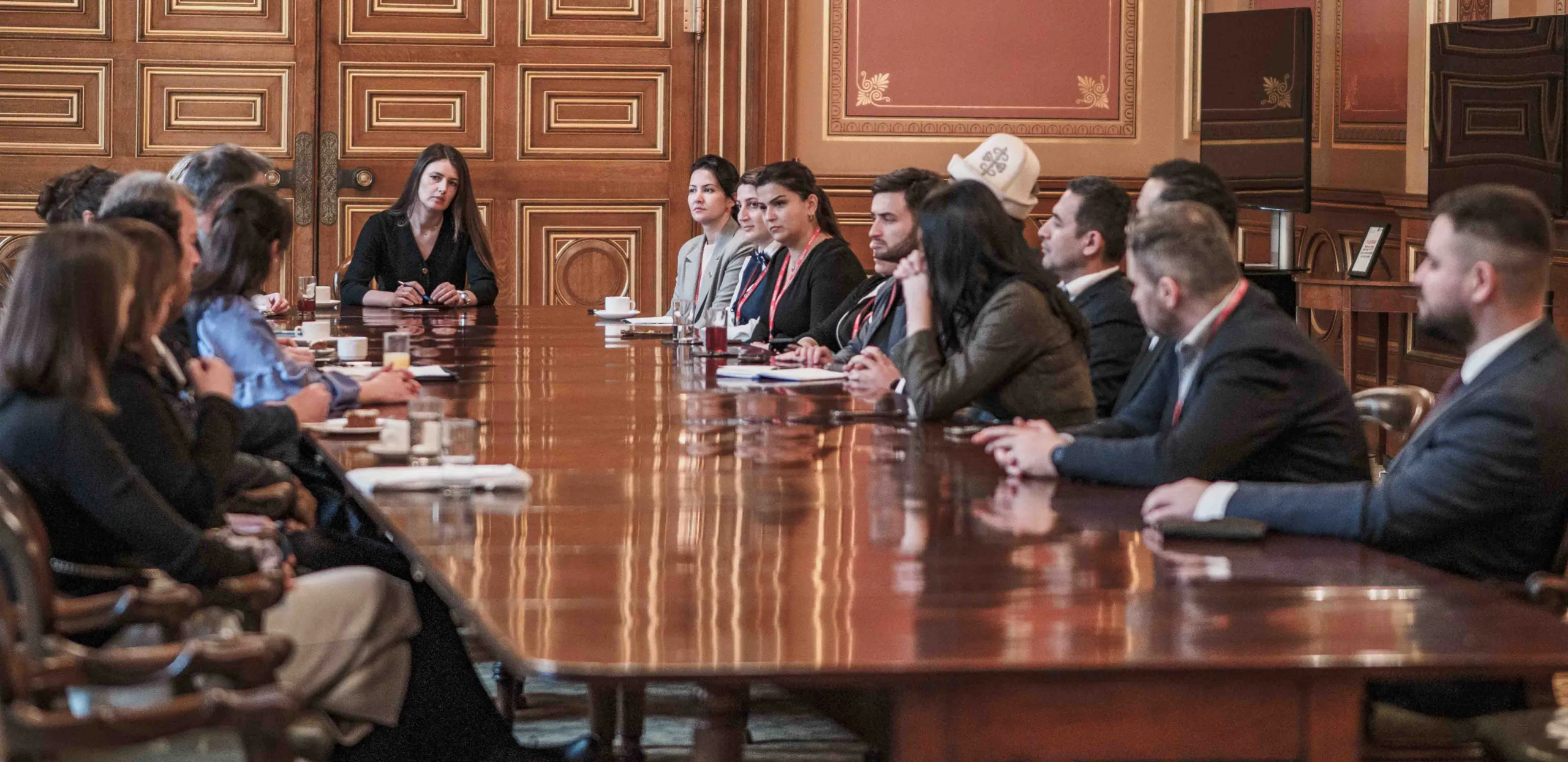 Fellows at a long table in a grand room with red walls