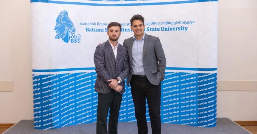 Giga and Dan at a conference in front of a banner
